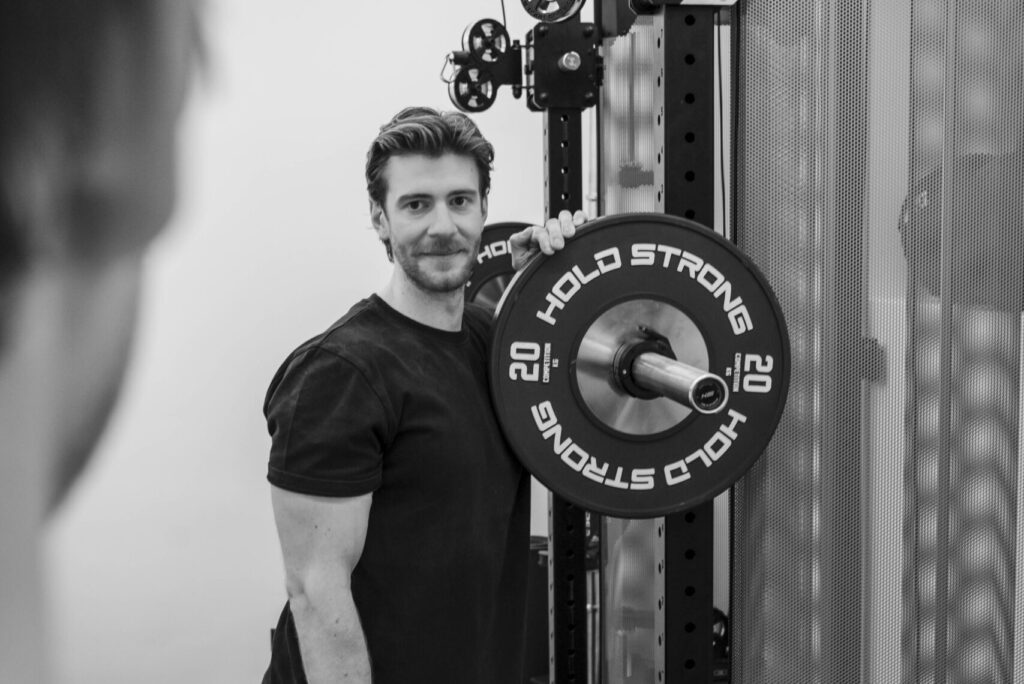 Daniel in der Physiotherapie in Bad Hofgastein. Er lehnt an einer Langhantel mit Gewichten.